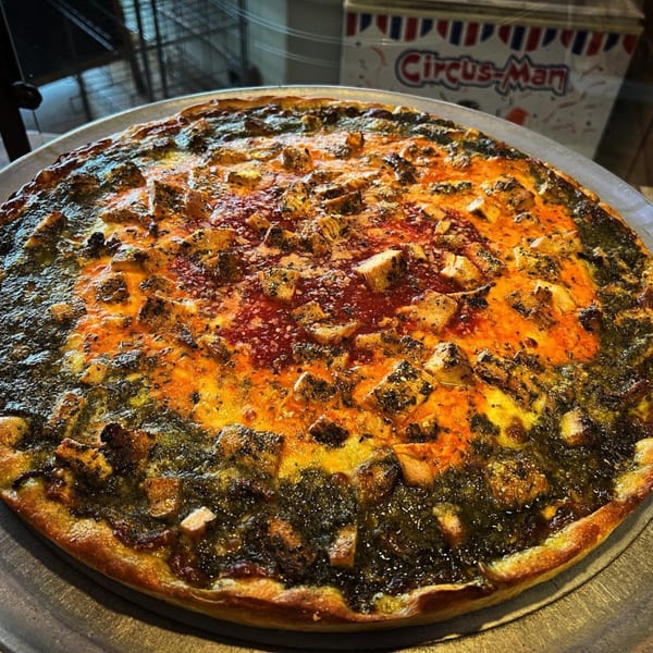 Luigi's Pizza's chicken pesto pizza with red sauce and cheese on a metal pan.