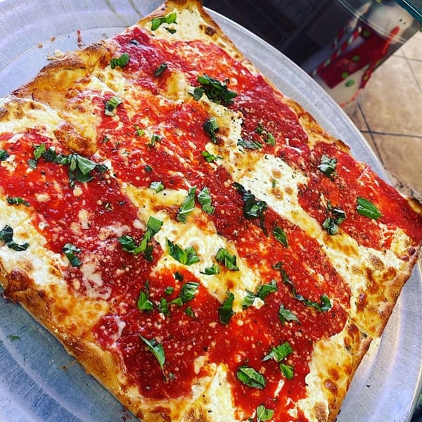 A square Luigi's Pizza with red sauce stripes, melted cheese, and fresh basil on a metal tray.