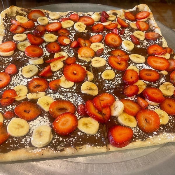 Luigi's Pizza dessert pizza with chocolate spread, sliced strawberries, bananas, and powdered sugar.