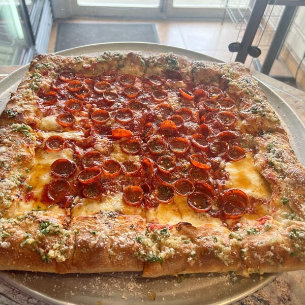 A large, rectangular pepperoni pizza from Luigi's Pizza, with a thick, cheesy crust, on a metal tray.
