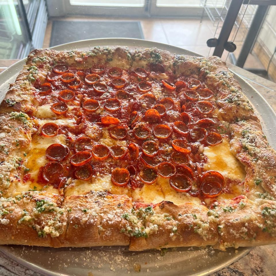 A large, rectangular pepperoni pizza from Luigi's Pizza, with a thick, cheesy crust, on a metal tray.