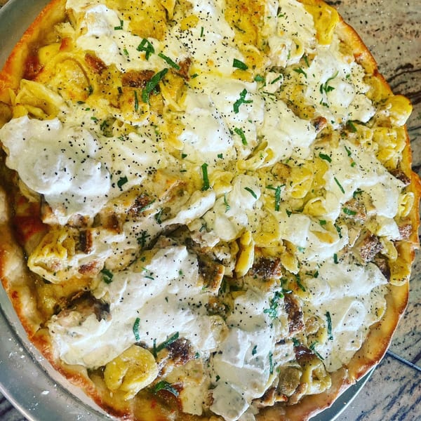 Luigi's Pizza's tortellini pizza, topped with creamy white sauce, black pepper, and fresh herbs.