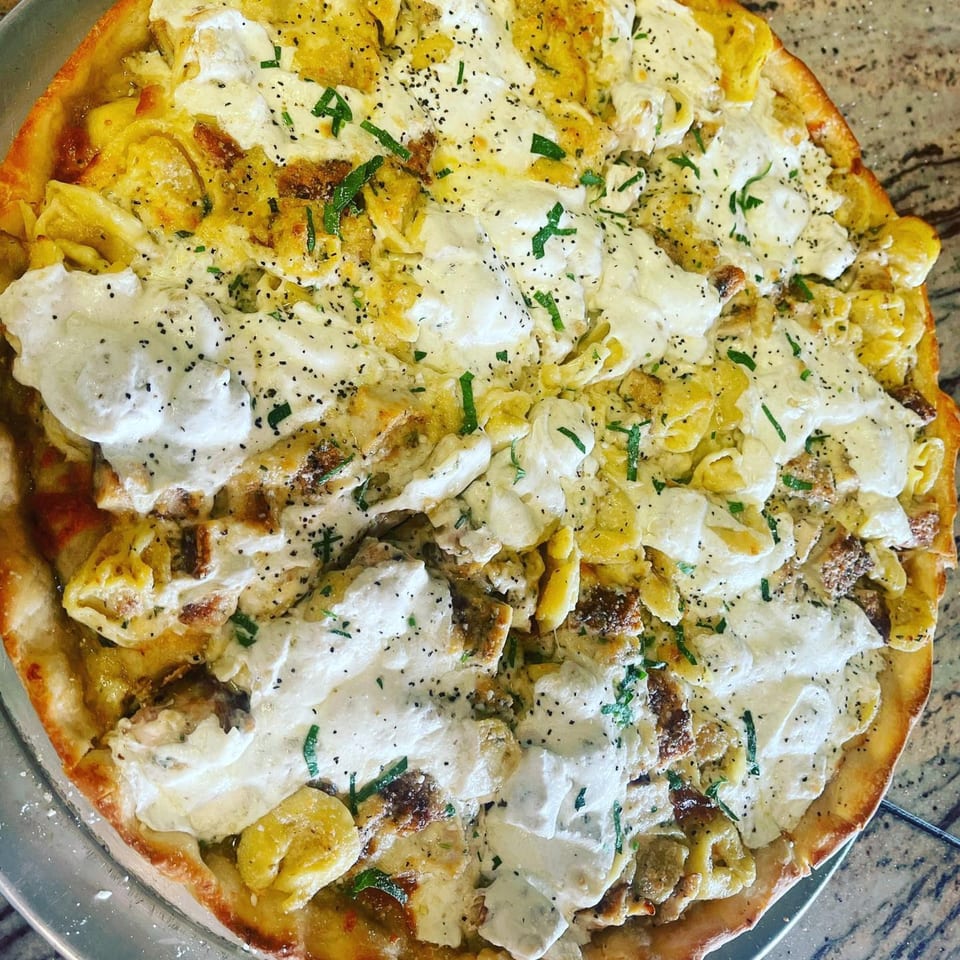 Luigi's Pizza's tortellini pizza, topped with creamy white sauce, black pepper, and fresh herbs.