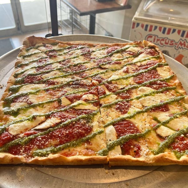 A rectangular Luigi's Pizza with red sauce, white cheese, and green pesto stripes on a metal tray.